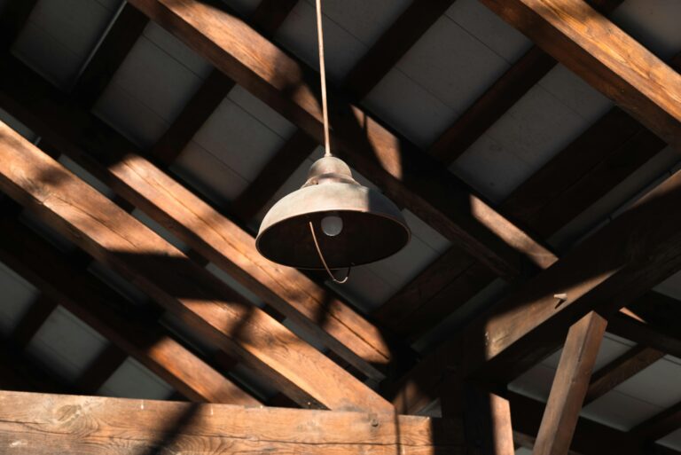 A rustic pendant lamp hanging from a wooden ceiling, illuminated by natural daylight casting shadows.